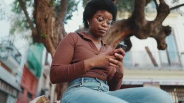 Gözlüklü Afrikalı bir kız ağacın altında otururken akıllı telefondan mesaj yazıyor. Dışarıda cep telefonunu kontrol eden genç bir kadın. Modern teknoloji