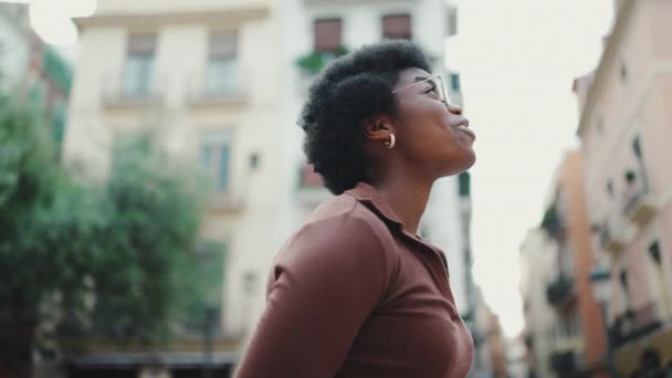 暗い髪のアフリカの女性の側のビューだけで路上に立って笑みを浮かべている 魅力的なアフリカの女の子の追跡ショット新しい都市を探索 — ストック動画
