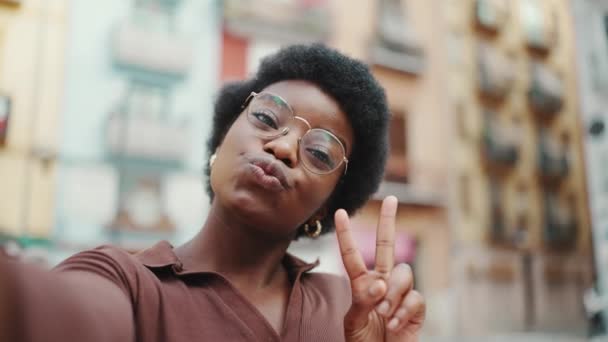 正面的非裔美国人黑头发女人在街上自拍 美丽的博客女孩在户外的相机上进行空中亲吻和表示和平姿态 — 图库视频影像