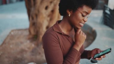 Gözlük takan güzel Afrikalı bir kız online alışveriş yaparken akıllı telefon kullanıyor. Açık havada cep telefonundan haber okuyan esmer tenli genç bir kadın.