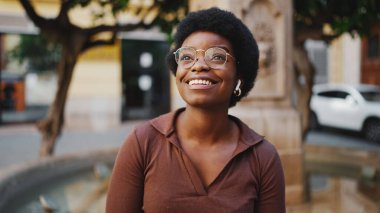 Açık havada iyi bir ruh hali içinde bir kadın. Afro-Amerikalı bir kadın sokakta oturmuş kulaklıkla müzik dinliyor.