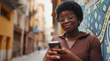 Güzel Afro kız akıllı telefonundan mesaj okuyor, gözlük takıyor. Dışarıda cep telefonu kullanan bir kadın.