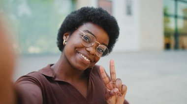 Çekici esmer kadın sokakta selfie çekerken barış jesti gösteriyor. Genç Afro kadın kameraya gülümsüyor