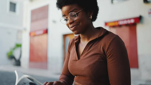 Afro woman wearing casual reading book and smiling on the street. Woman in a relaxed mood reading book outdoors