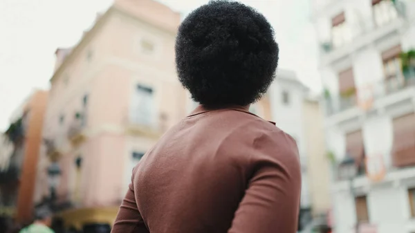 Back view of dark haired African woman standing on a street. Attractive Afro girl exploring new city alone
