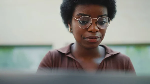 Close up Afro curly haired woman in glasses looking serious working on laptop. Young businesswoman working outdoor