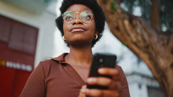 Vakker Afro Jente Som Sjekker Mobilen Utendørs Med Briller Ung stockbilde