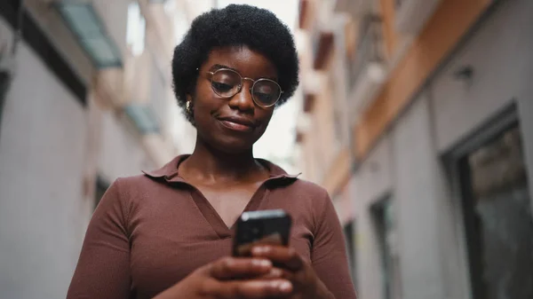 Ung Afrojente Med Briller Som Sms Smarttelefon Kvinnelig Kontroll Mobiltelefonen stockbilde