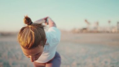 Spor giyim bölümünde genç bir kadın plajda vücudunu yogaya hazırlıyor. Dişi yogi dışarıda pratik yaparken kendinden emin görünüyor.