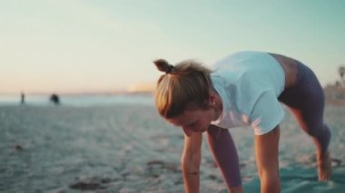 Spor elbiseli, şık görünümlü genç bir kadın sahilde yoga egzersizi yapıyor. Güzel kız dışarı çıkıyor.