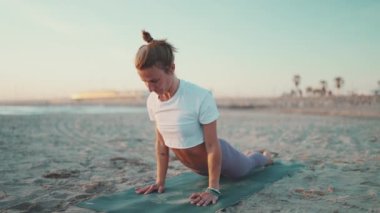 Genç, dövmeli, spor görünümlü, yoga yapan ve plajda esneme hareketleri yapan bir kadın. Yoga sınıfında kadın yogi.