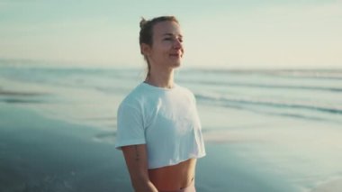 Yoga antrenmanından sonra deniz kenarında yürürken mutlu görünen çekici sarışın kadın. Sportif kız sahilde sabahın tadını çıkarıyor.