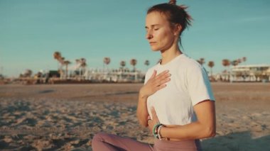 Şehvetli bir kadın gözlerini kapalı tutuyor lotus pozisyonunda oturuyor ve deniz kenarında meditasyon yapıyor. Yoga dersi sırasında dışarıda düzgün nefes alma pratiği yapan genç yoga öğretmeni.