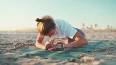 Sportif kadın dışarıda yoga minderinde ısınma egzersizi yapıyor. Genç yoga öğretmeni plajda yoga antrenmanı yaparken geriniyor.