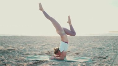 Güzel bir poz, yoga yapan şık bir kadının sahilde bacaklarını açtığı bir poz. Yoga hocası dışarıda minderde yoga yapıyor.
