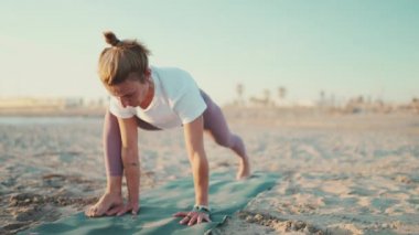 Paspasın üzerindeki güzel, sağlıklı kadın ısınma egzersizi yapıyor. Genç yoga öğretmeni plajda yoga antrenmanı yaparken geriniyor.