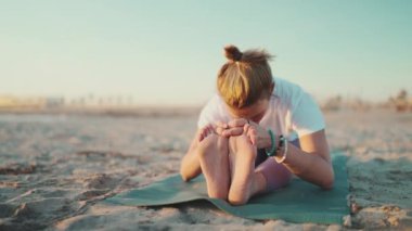 Genç ve güzel bir kadın dışarıda yoga egzersizi yapıyor. Yoga öğretmeni, sabah yoga dersinde paspas üzerinde egzersiz yapıyor.