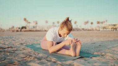 Açık havada yoga egzersizi yapan formda bir kadın. Çekici bir kadın plajda hasırla egzersiz yapıyor. Sabah yoga dersi.