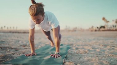 Havalı sarışın kadın deniz kenarında spor minderinde yoga yapıyor. Spor kıyafetli çekici yogi kızı sabah plajda kobra pozu veriyor.