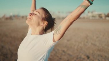 Kapalı dövmeli kadın mutlu görünüyor. Sahilde yoga antrenmanının keyfini çıkarıyor.