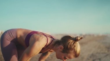 Spor giyimli şık sarışın kadın sahilde sabah yogasının tadını çıkarıyor. Çekici dövmeli kız deniz kenarında geriniyor.