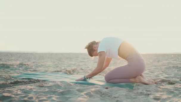 屋外でヨガの演習を行う魅力的な女性 ビーチでマットストレッチボディで運動する若いヨギ女 朝ヨガ — ストック動画