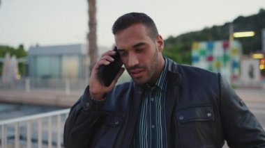 Deri ceket giymiş, kendine güvenen genç iş adamı dışarıda akıllı telefondan konuşuyor. Sokakta cep telefonu kullanan yakışıklı bir adam. Telefon görüşmesi