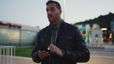 Yakışıklı esmer adam, akşam arkadaşlarıyla buluşmaya giderken akıllı telefon kullanarak kendinden emin görünüyor. Çekici adam açık havada telefonu kontrol ediyor.