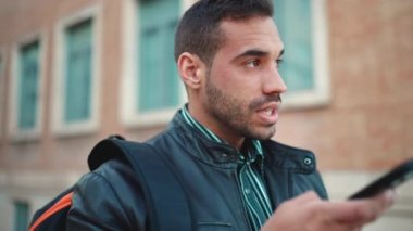 Açık havada akıllı telefondan sesli mesaj kaydeden çekici esmer adamın portresi. Sokaktaki genç adam iletişim için cep telefonunu kullanıyor.