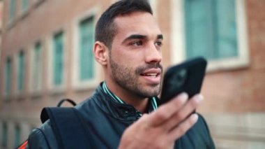 Açık havada akıllı telefon kullanarak arkadaşına sesli mesaj kaydeden esmer adamı kapat. Güzel bir adam sokakta dikiliyor ve hoparlörden konuşuyor.