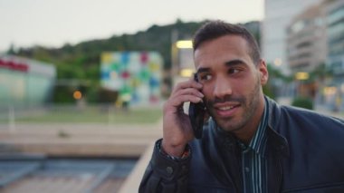 Açık havada esmer bir adam akıllı telefon kullanarak kız arkadaşıyla konuşuyor. Çekici adam telefonda konuşuyor. Akşam sokakta yürürken.