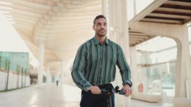 Çizgili gömlekli genç yakışıklı işadamı açık hava iş toplantısına elektrikli scooterla giderken kendinden emin görünüyor.