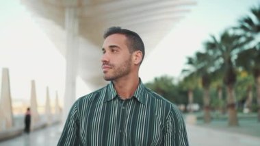 Çizgili tişört giymiş yakışıklı kaslı adam dışarıda kendinden emin görünüyor. Genç adam caddede yürüyor ve kameraya gülümsüyor.