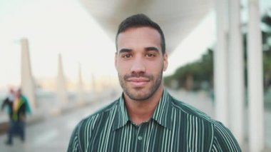Yakından, çizgili gömlek giyen güzel esmer adamın kameraya güvenle baktığı ve açık havada gülümsediği bir fotoğraf. Yüz ifadesi