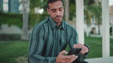 Tişörtlü yakışıklı bir işadamı sokakta akıllı telefonuyla iş e-postalarını kontrol ediyor. Genç girişimci dışarıda çalışırken düşünceli görünüyor.
