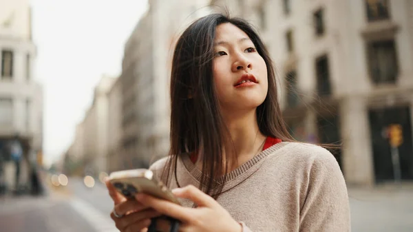 在独自探索新城市的同时 梦幻般的亚洲女人看起来很沉思 亚洲女性游客手拿着智能手机沿着美丽的街道走着 — 图库照片