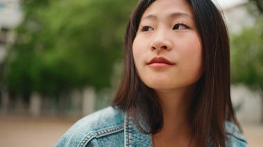Uzun saçlı Asyalı kadın dışarıda yalnız dinlenirken dalgın görünüyor. Güzel Japon kız sokakta oturuyor.