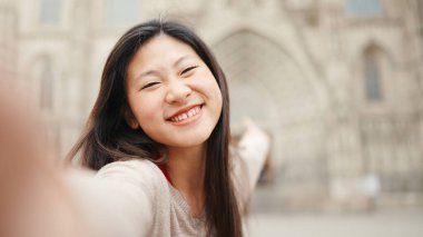 Neşeli esmer Asyalı kız eski mimarinin arka planında selfie çekerken samimi bir şekilde gülümsüyor. Japon kadın güzel bir gün geçiriyor.