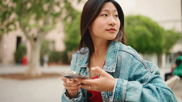 长发亚洲女人穿着配有智能手机的斜纹棉布夹克 寻找必须来的朋友 迷人的女孩在户外休息 — 图库照片