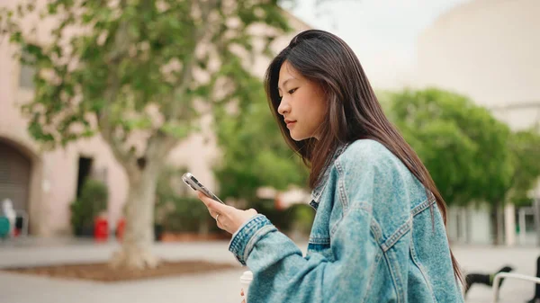在街上等朋友时 身穿斜纹棉布夹克的美丽的长发亚洲女孩在社交媒体上的侧面照片 — 图库照片