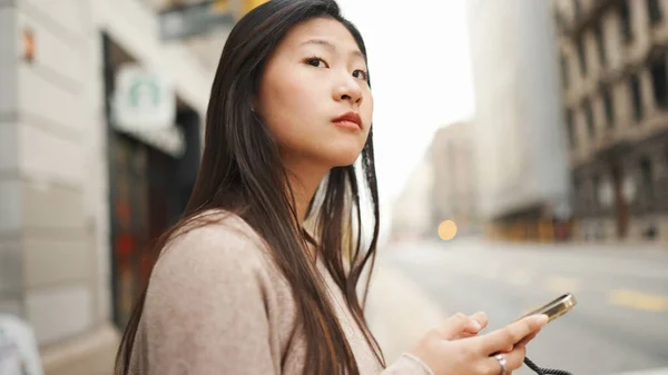 在侧面拍摄的照片中 长长的头发亚洲女人聚精会神地拿着智能手机走过人行道 日本女孩的户外肖像 — 图库照片