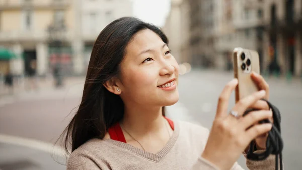 在街上用智能手机拍照时 相当长头发的亚洲女人看上去很高兴的样子 新来乍到 — 图库照片