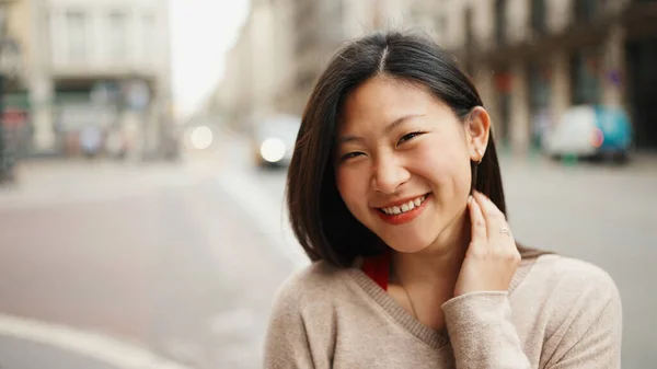 Portrait of cheerful Asian woman looking at camera and smiling standing on the city street. Happy emotions