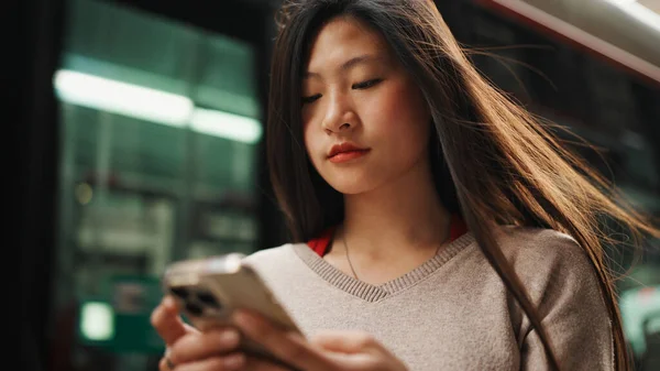 Kaunis Aasialainen Pitkätukkainen Nainen Etsii Oikeaa Kohdetta Älypuhelimella Seisoo Bussiasemalla — kuvapankkivalokuva