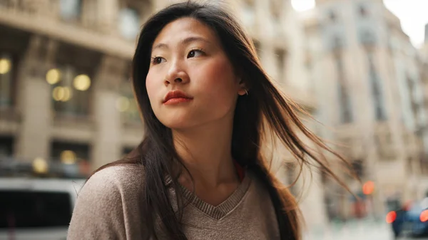 Pensive Asian long haired woman looking aside standing on the street alone. Pretty Asian girl exploring new city