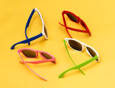 Sarı arkaplanda renkli çerçeveleri olan modern plastik güneş gözlükleri