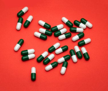 Kırmızı arka planda reçeteli ilaç kapsülleri yığını