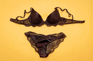 Sarı arka planda izole edilmiş siyah dantelli sutyen ve külot.