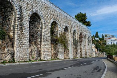 Empty rural road next to stone arches wall on the side during day