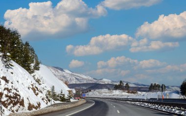 Empty highway road among tall mountains covered with snow and blue sky in the back